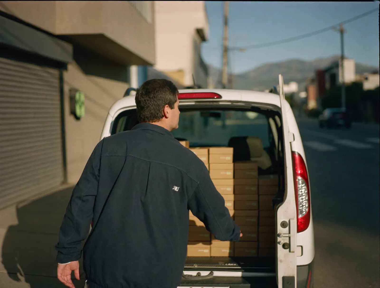 Conductor junto a un furgón de reparto con cajas ordenadas en filas, en una calle de Santiago al atardecer